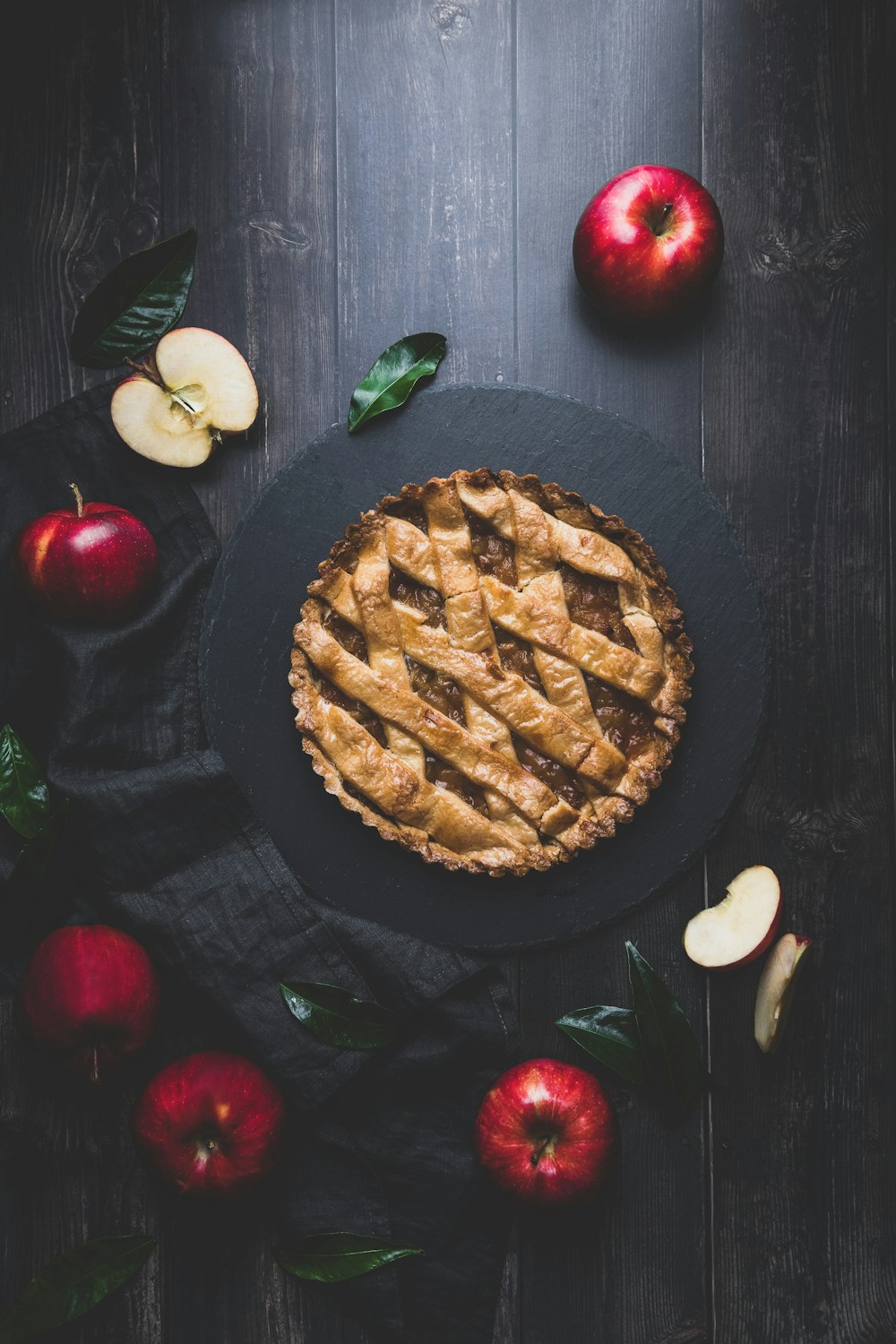 an apple pie on a black plate surrounded by apples