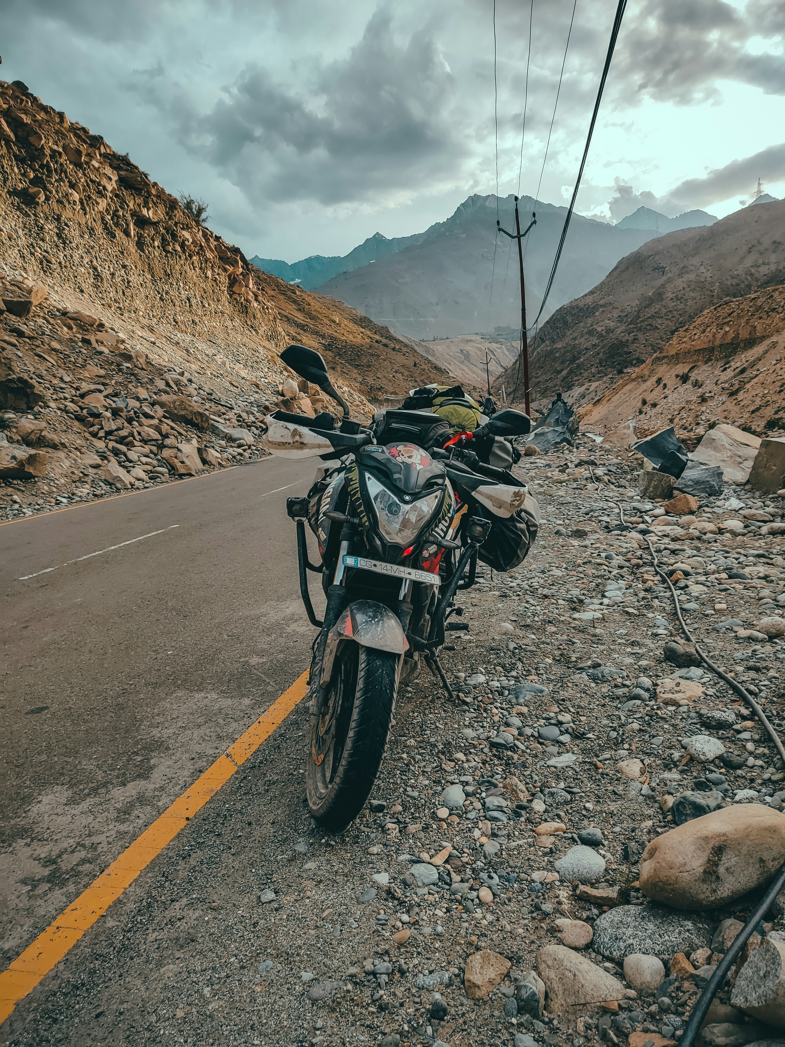 Motorcycle on remote Spiti Valley road, snow peaks, dramatic overcast sky, isolation