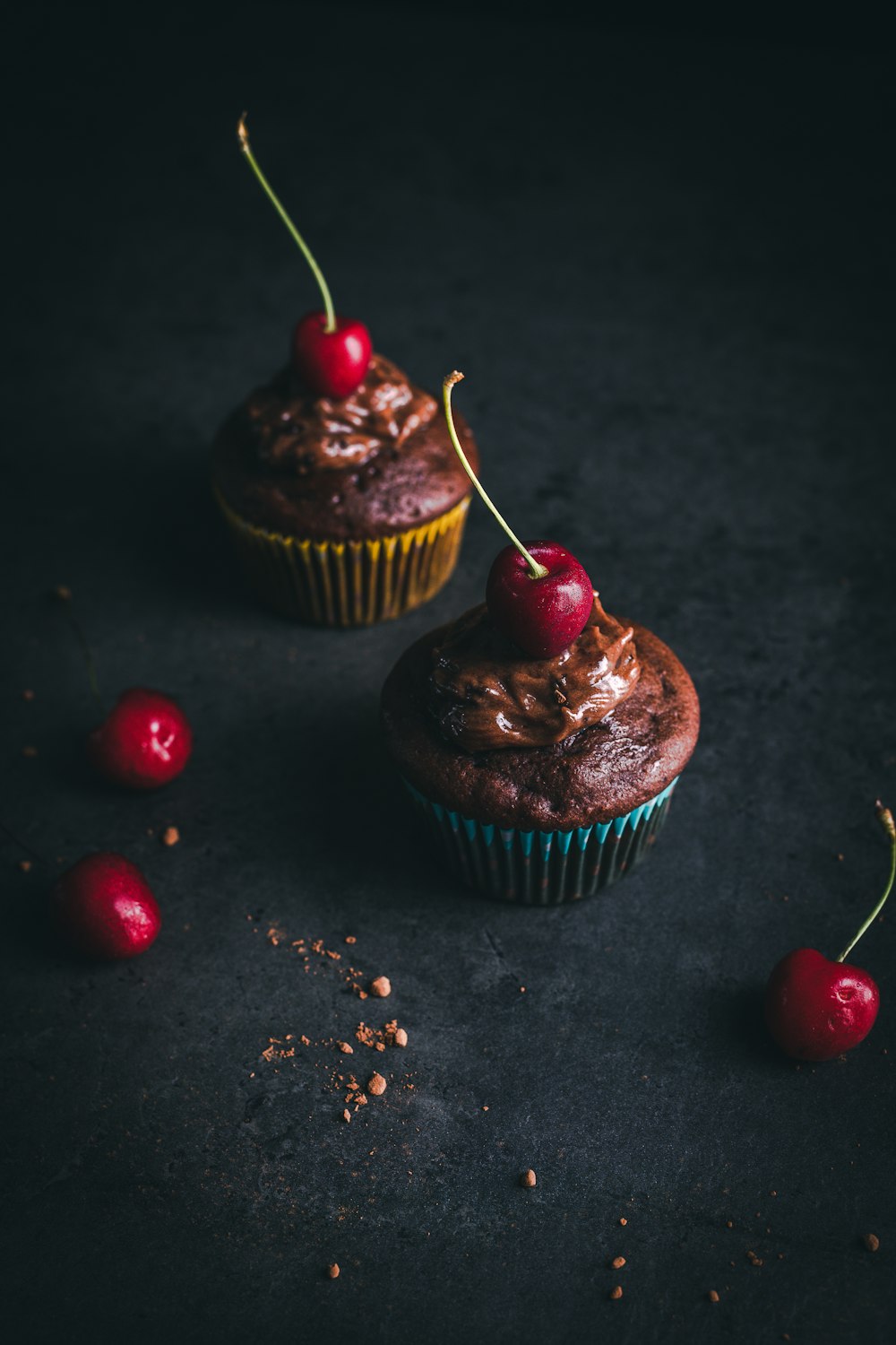 two cupcakes with chocolate frosting and cherries