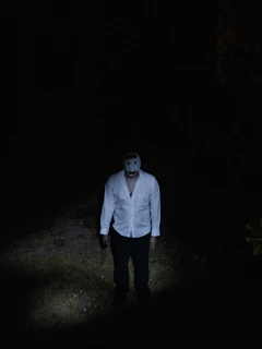 A mysterious figure wearing a bold mask and collar, bathed in deep shadows with a single spotlight.