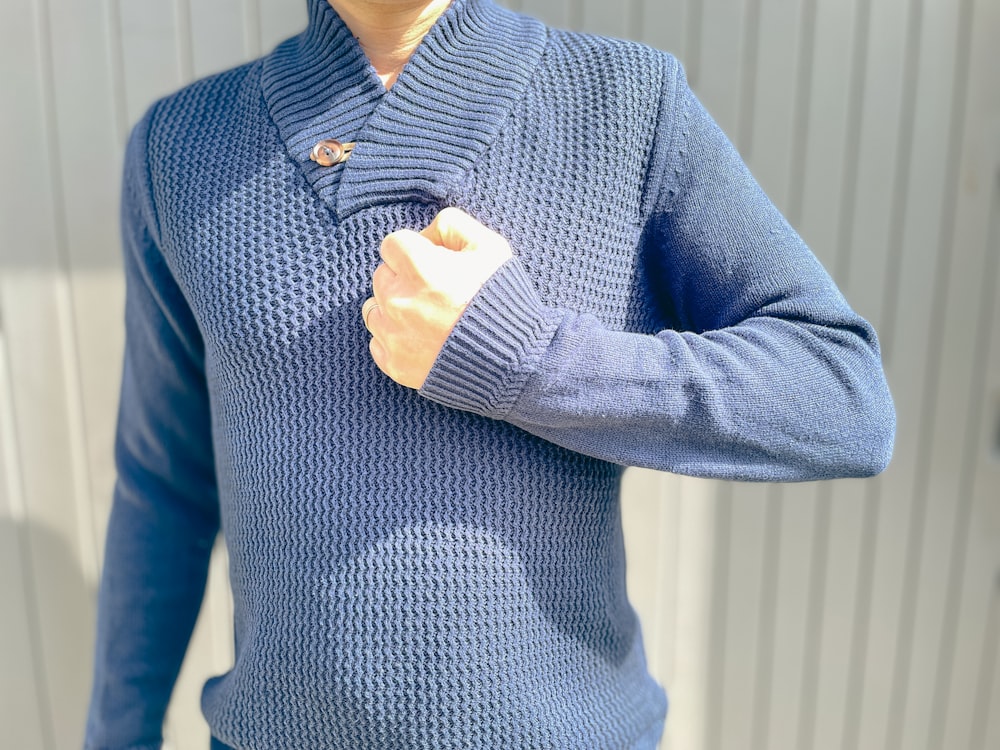 Una persona che indossa un maglione blu e tiene in mano un controller Wii