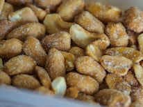 Close-up shot of roasted peanuts coated with coarse salt, showing crunchy textures and a warm, golden brown color.