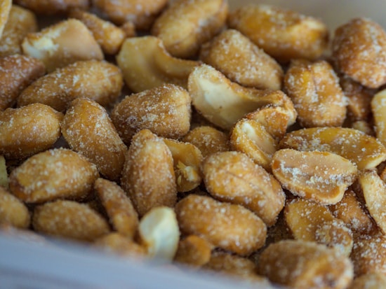 Close-up shot of roasted peanuts coated with coarse salt, showing crunchy textures and a warm, golden brown color.