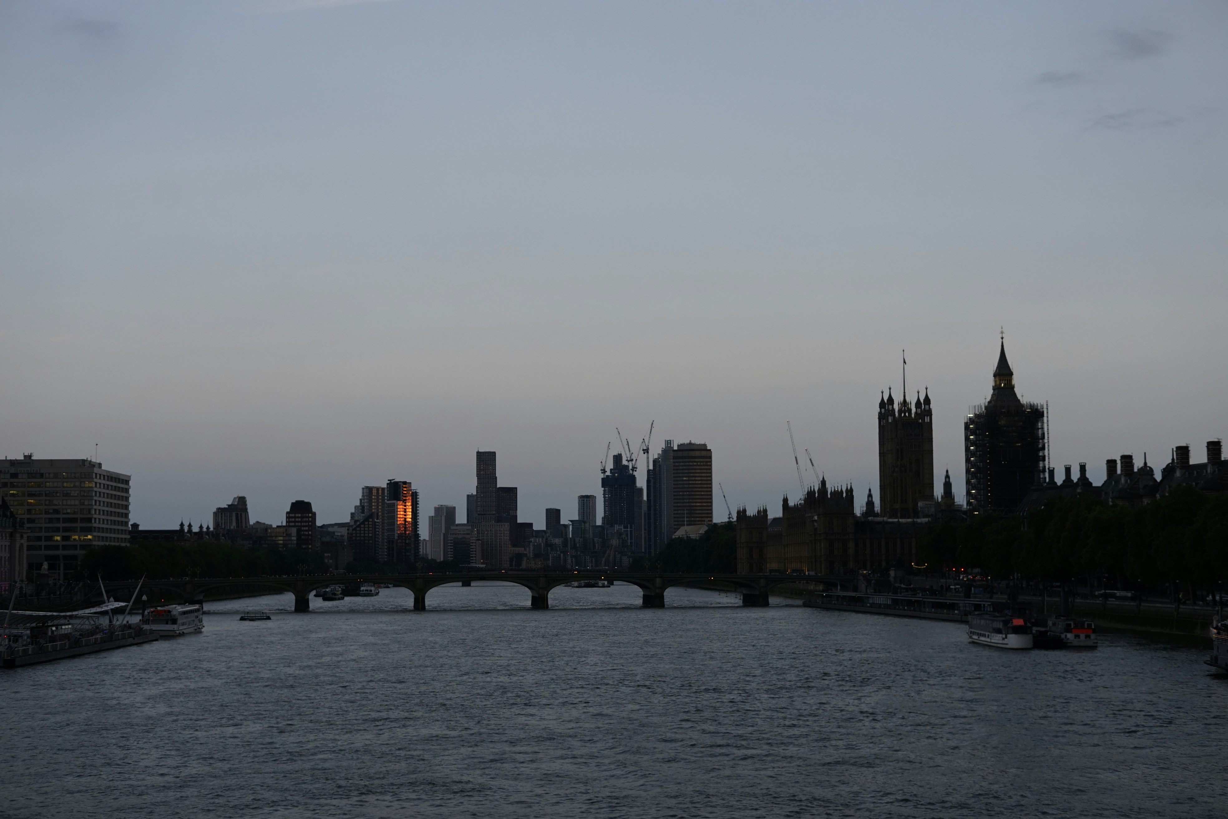 London skyline at dusk, Tower Bridge silhouette against deep navy sky, dark Thames river below, moody atmospheric fog, dramatic low-key lighting