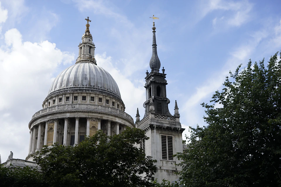 Majestic white and gray stone building with dome stands on street corner surrounded by trees