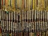 An array of colorful beads is hanging, forming an intricate and dense pattern. The beads are strung together in varying colors and sizes, showcasing a rich variety of earthy tones and vibrant highlights.