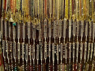 An array of colorful beads is hanging, forming an intricate and dense pattern. The beads are strung together in varying colors and sizes, showcasing a rich variety of earthy tones and vibrant highlights.