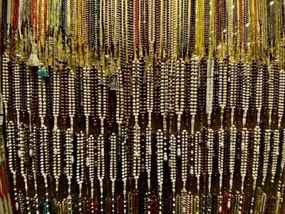 An array of colorful beads is hanging, forming an intricate and dense pattern. The beads are strung together in varying colors and sizes, showcasing a rich variety of earthy tones and vibrant highlights.
