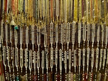 An array of colorful beads is hanging, forming an intricate and dense pattern. The beads are strung together in varying colors and sizes, showcasing a rich variety of earthy tones and vibrant highlights.