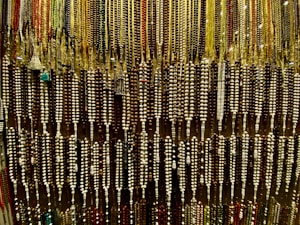 An array of colorful beads is hanging, forming an intricate and dense pattern. The beads are strung together in varying colors and sizes, showcasing a rich variety of earthy tones and vibrant highlights.