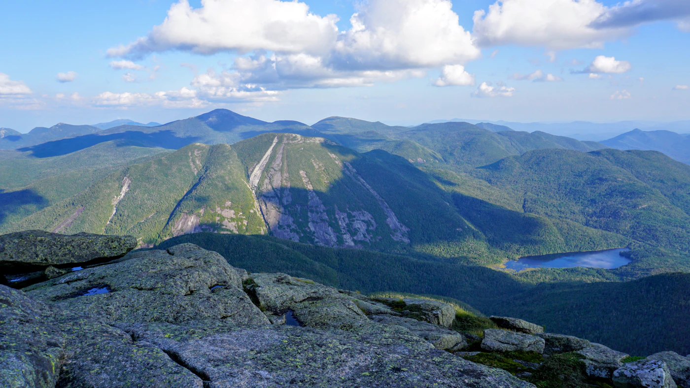 Open rock summit in the Adirondack High Peaks looking out over a forested range and a lake below