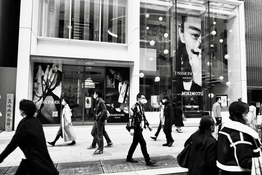 a black and white photo of people walking in front of a store