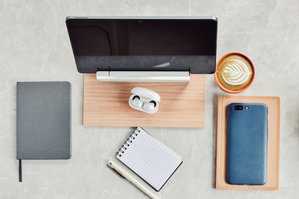 a desk with a laptop, notepad, cell phone and a cup of coffee