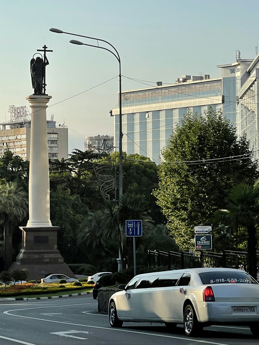 a white car driving down a street next to a tall statue