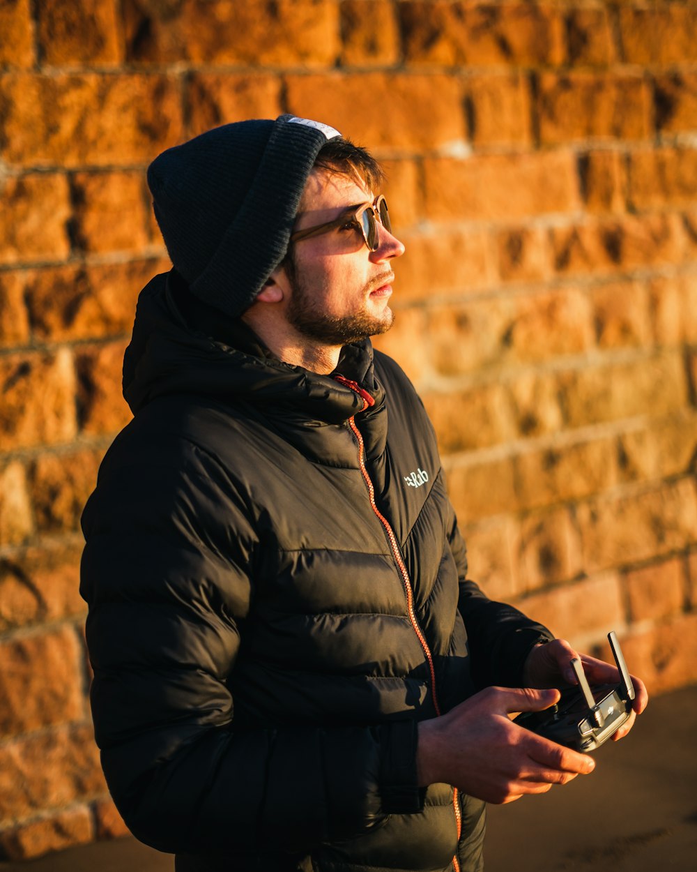 Ein Mann steht vor einer Ziegelmauer und hält ein Handy in der Hand