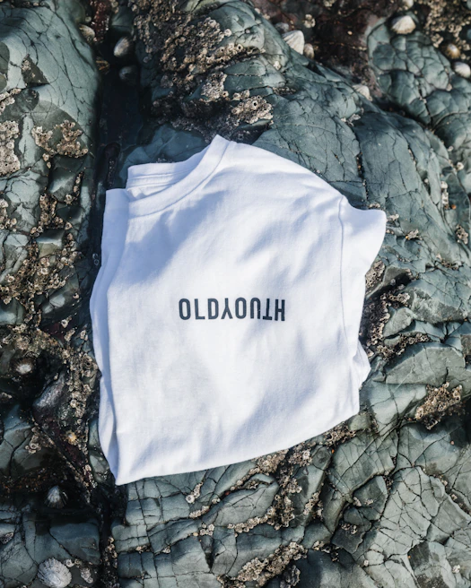 A black t-shirt laid flat on a white surface, featuring a minimalist poetic quote in English