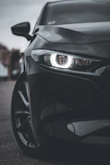 Close-up of a glossy black BMW with a newly installed front bumper and LED headlights shining brightly.