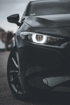 Close-up of a glossy black BMW with a newly installed front bumper and LED headlights shining brightly.