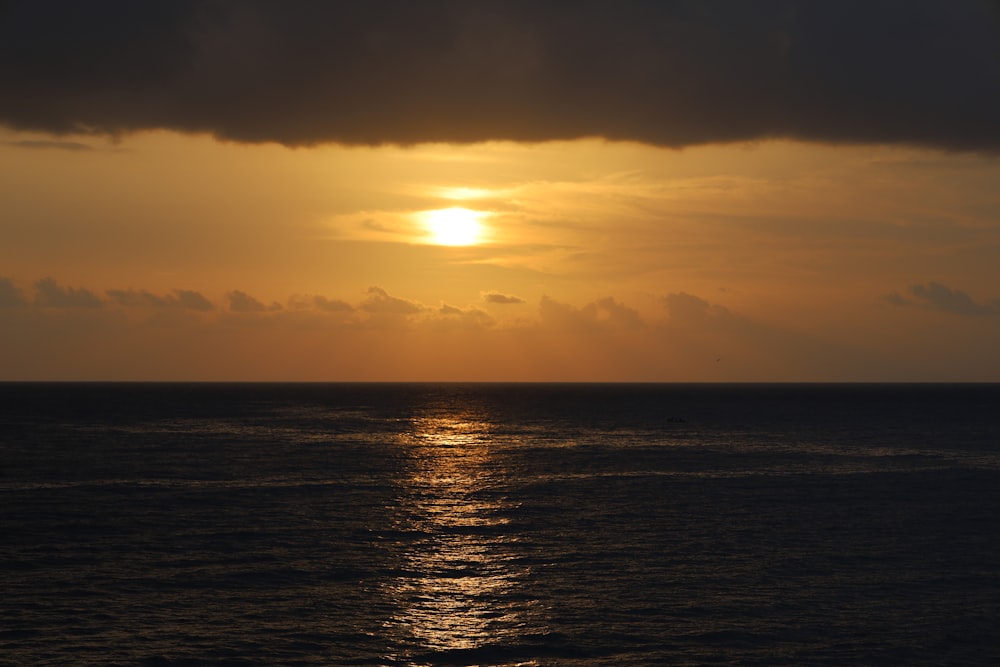 the sun is setting over the ocean on a cloudy day