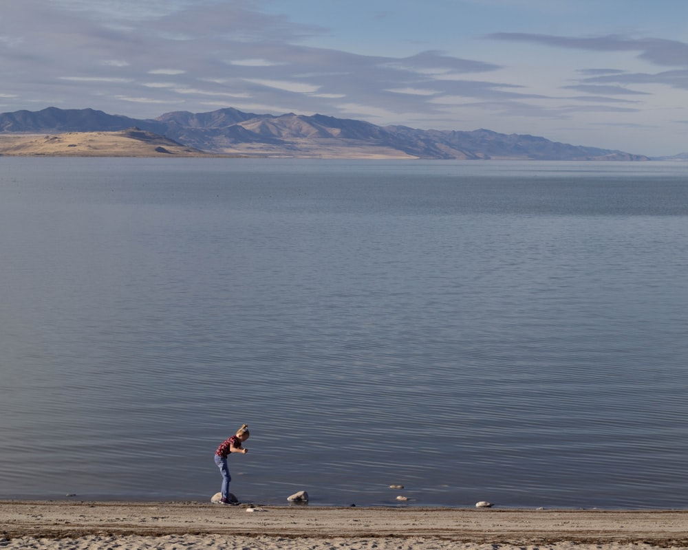 a woman standing on a beach next to a body of water