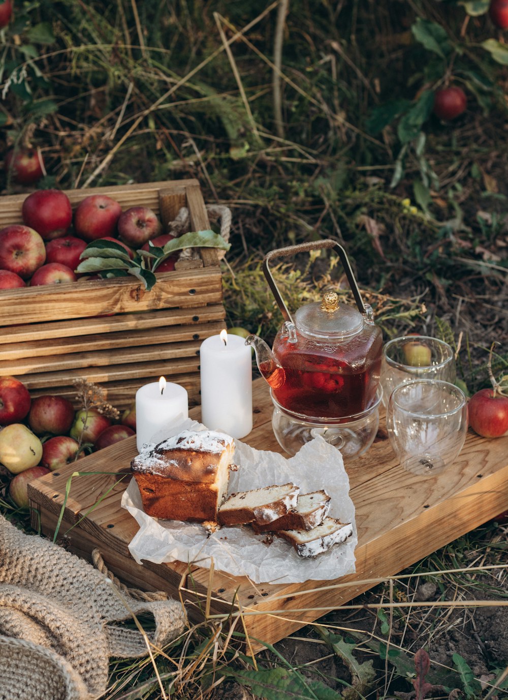 a wooden tray topped with a slice of cake next to a basket of apples