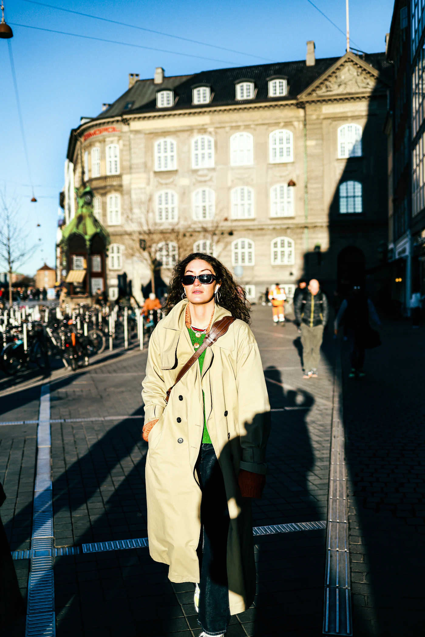 Woman walking in a beige trench coat layered over a green knit