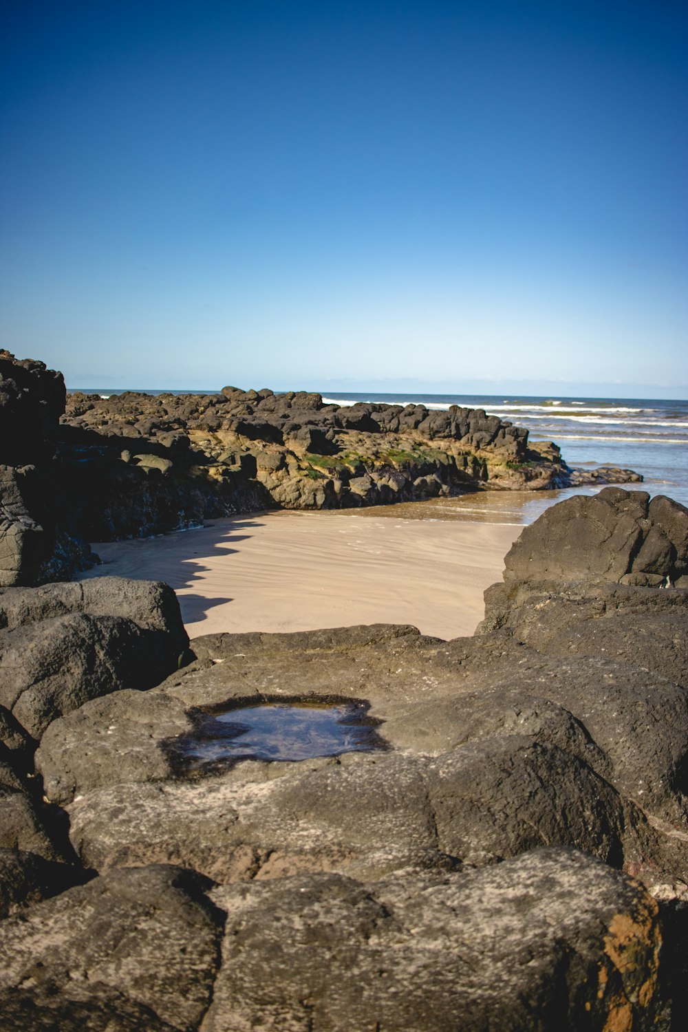 a rocky beach with a puddle of water in the sand