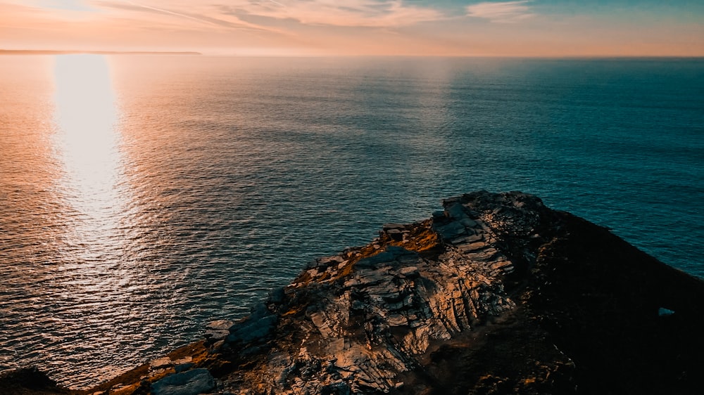 the sun is setting over the ocean with a rock outcropping