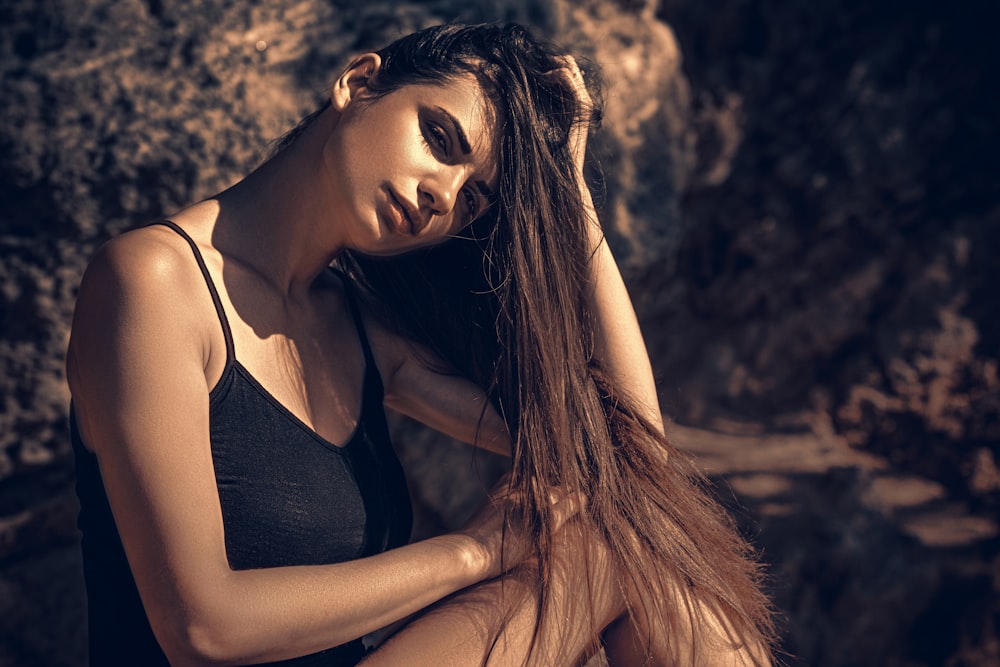 a woman with long hair sitting on a rock