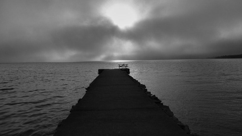 a black and white photo of a bench on a pier