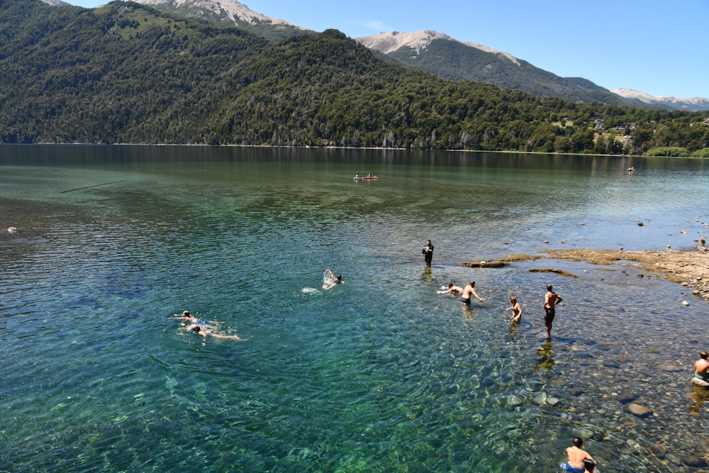 a group of people swimming in a lake with mountains in the background