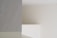 A minimalist interior scene with soft lighting, featuring a smooth marble surface on the left with subtle gray veining. The background consists of plain, neutral-colored walls creating shadows and depth.