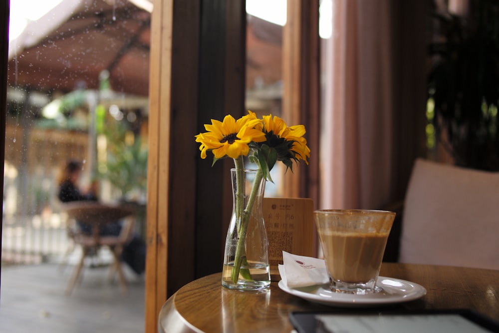 a vase of yellow flowers sitting on a table next to a cup of coffee