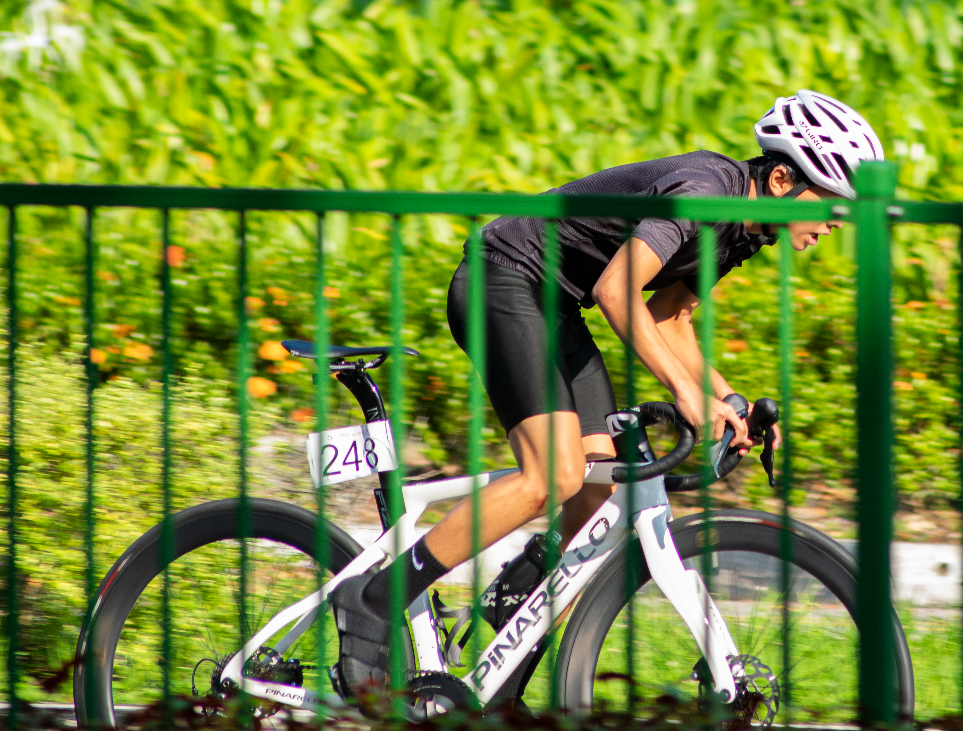a man riding a bike down a street next to a green fence