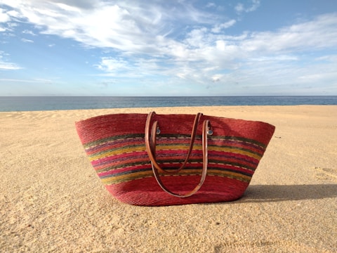 A collection of bamboo bags displayed on a sandy beach with ocean waves in the background.