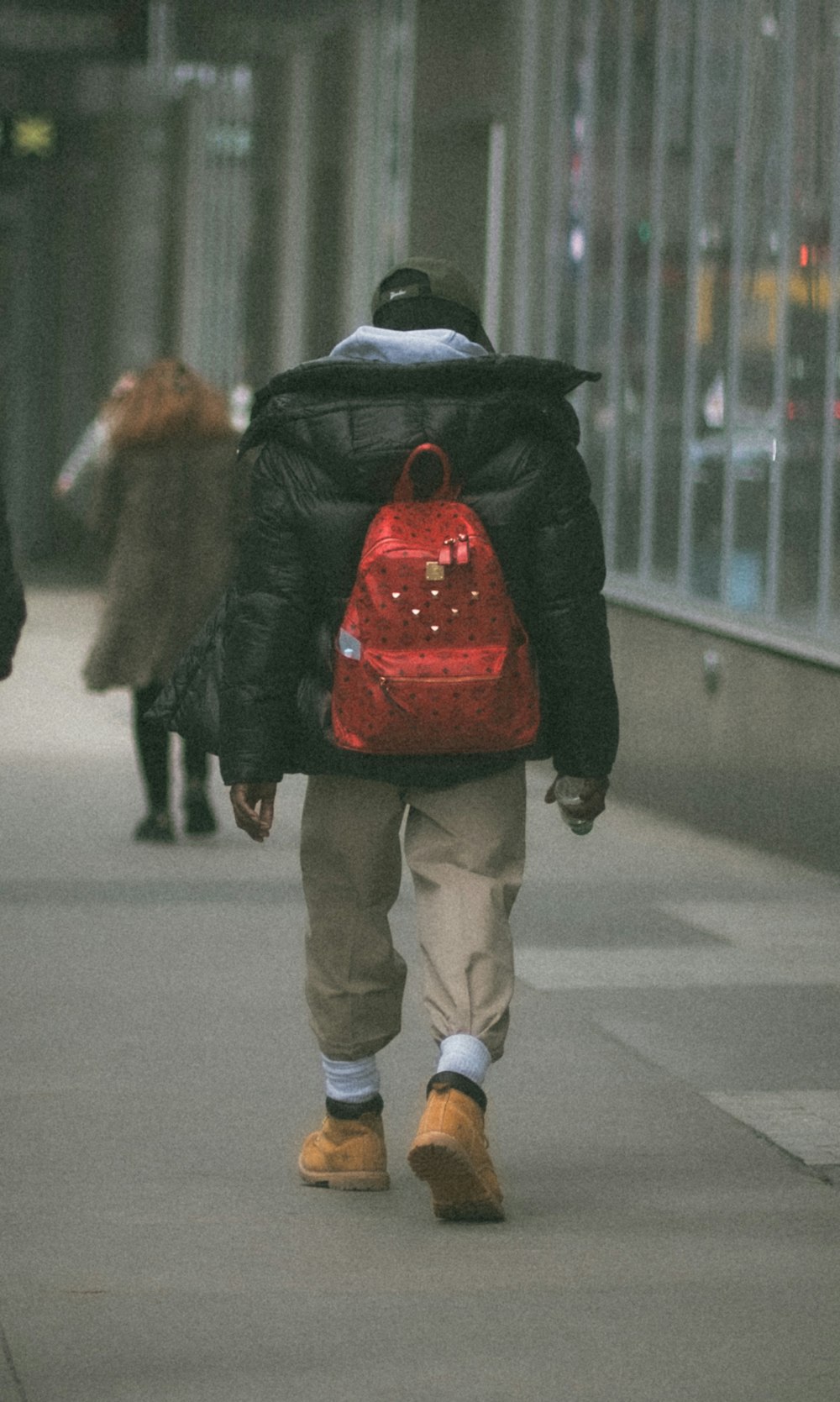 uma pessoa andando por uma calçada com uma mochila vermelha