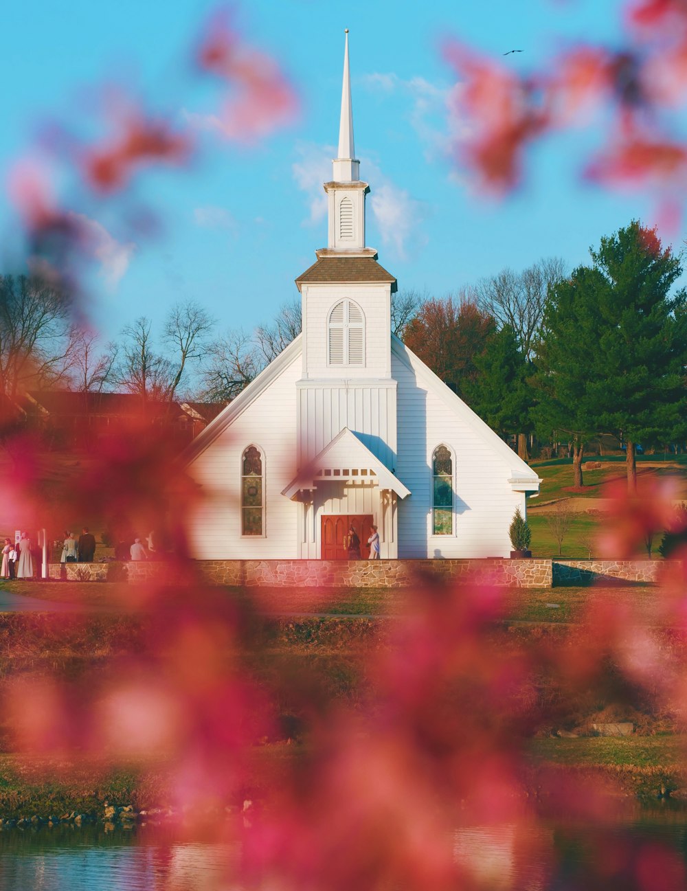 a church with a white steeple and a lake in front of it