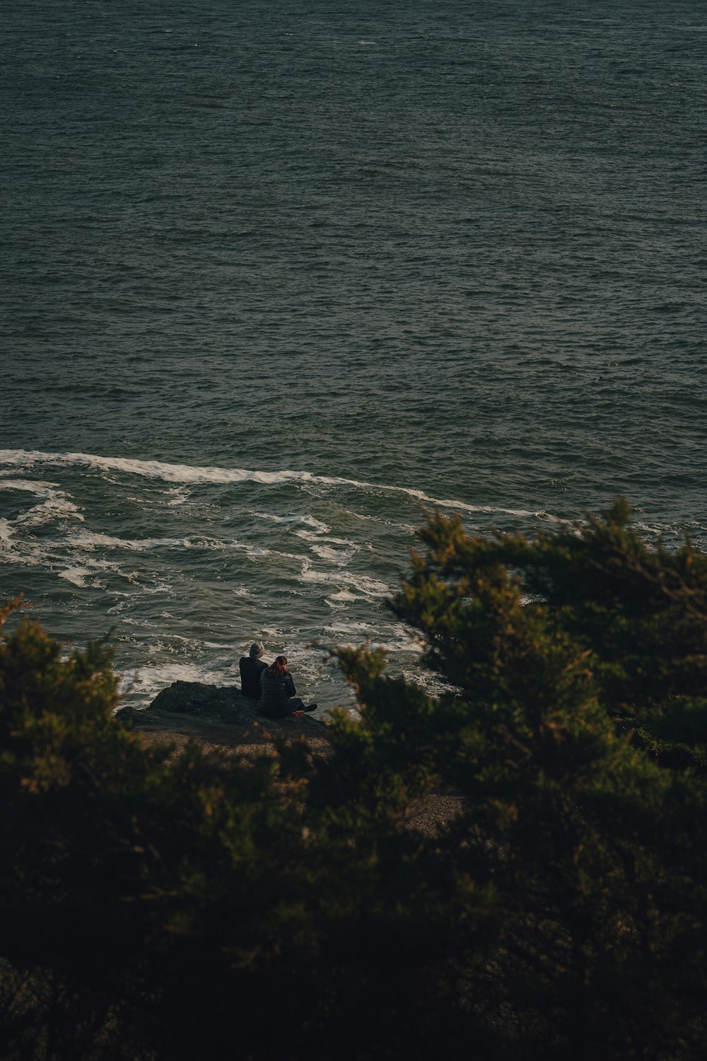 a couple of people sitting on top of a rock near the ocean