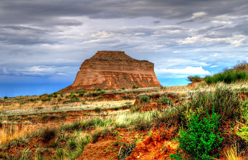 A lone sandstone butte standing above dry grassland under a wide evening sky
