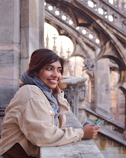 a smiling woman leaning on a wall with a building in the background