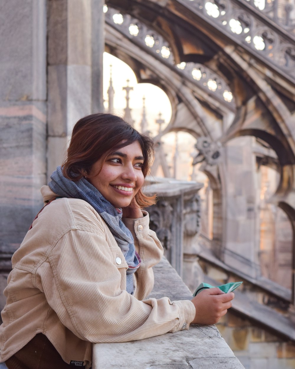 a smiling woman leaning on a wall with a building in the background