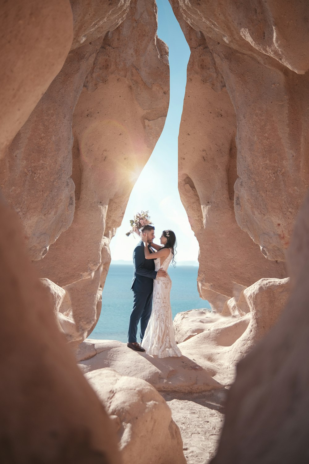 a bride and groom standing in between two large rocks