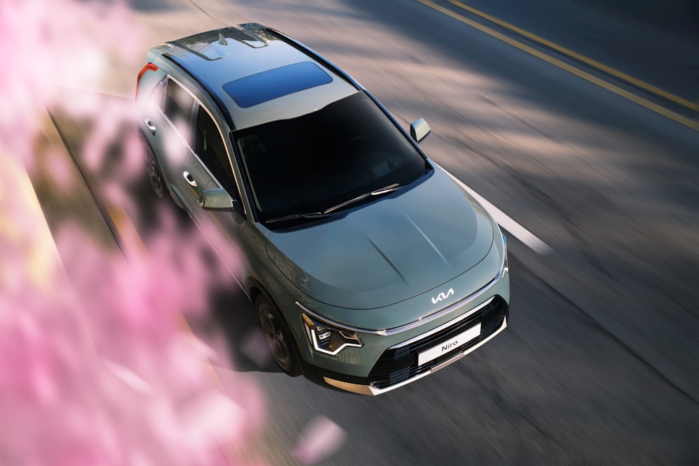 a silver car driving down a street next to pink flowers