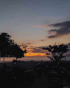 A serene Bali beach at sunset with a silhouette of a scooter parked nearby, capturing the island's laid-back vibe.