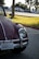 A classic car with a rounded shape is parked on the side of a road in a sunlit area with grass and trees in the background. It features a California license plate and has a maroon color with chrome accents.