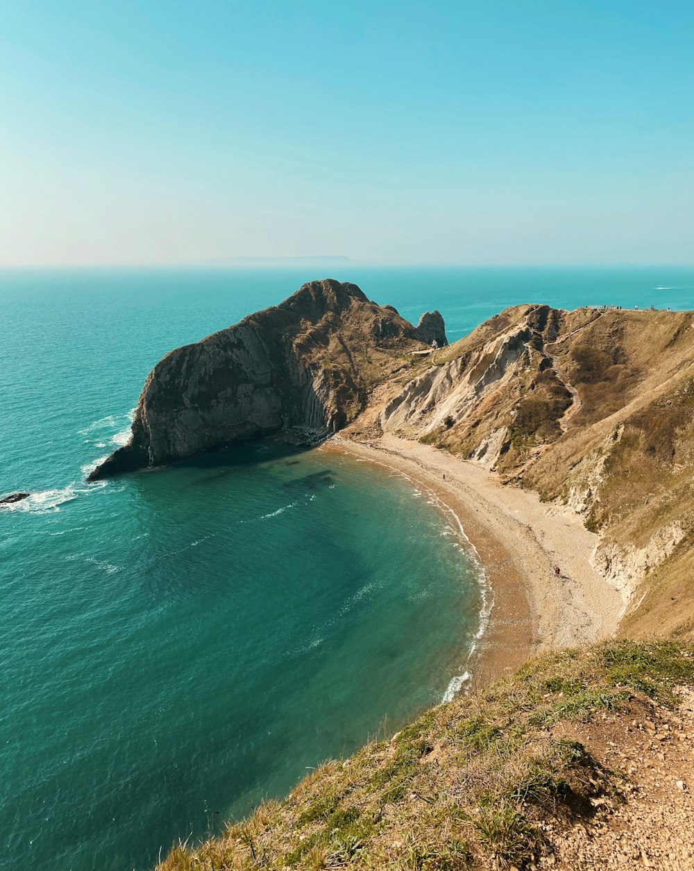 a beach with a cliff and water with Cabo de la Vela in the background