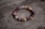 A bracelet made of polished beads in various shades of brown, red, and purple is placed on a textured wooden surface with a natural, rustic appearance. The beads are shiny and have a smooth finish, strung together in a circular arrangement.