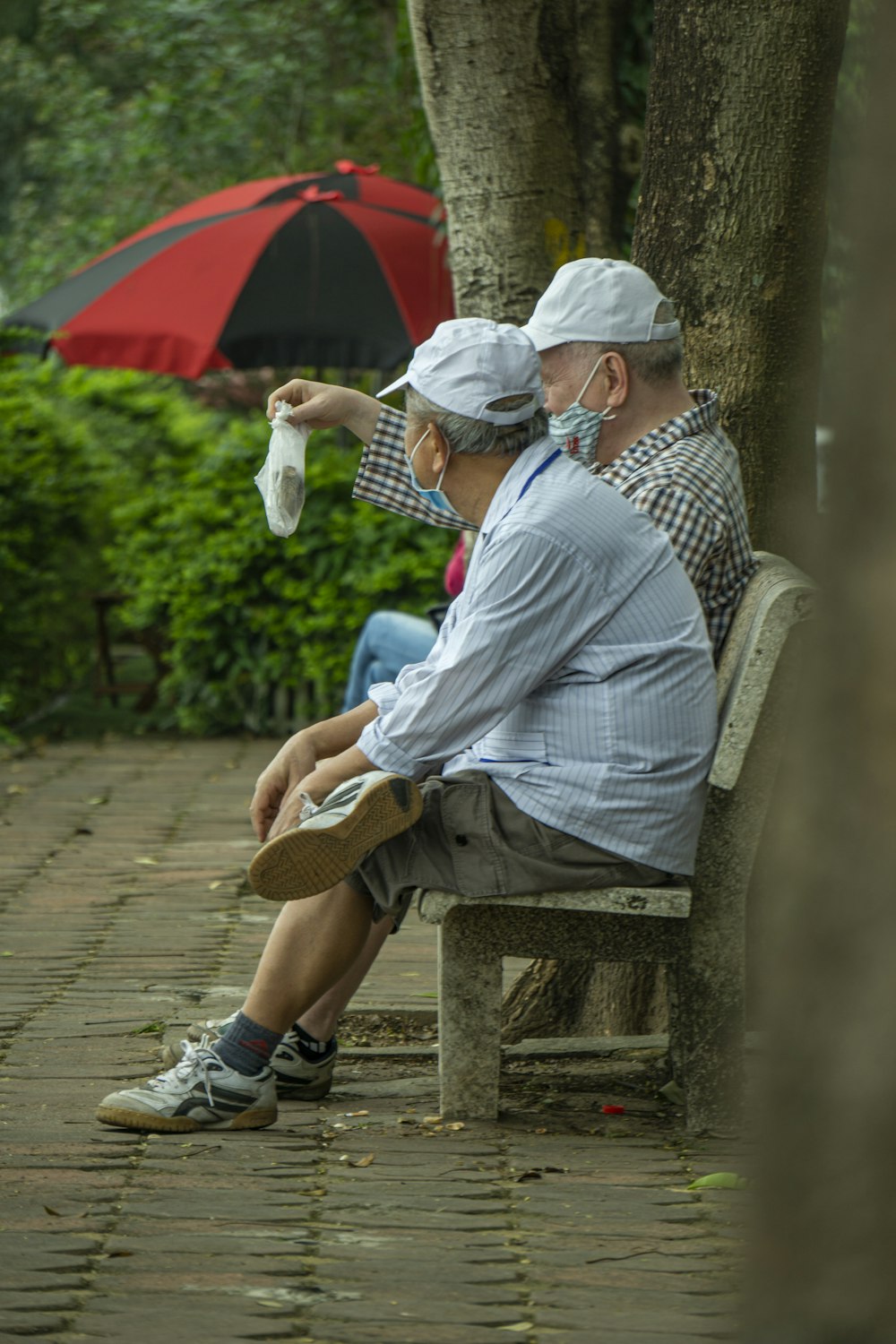 a couple of people sit on a bench under an umbrella