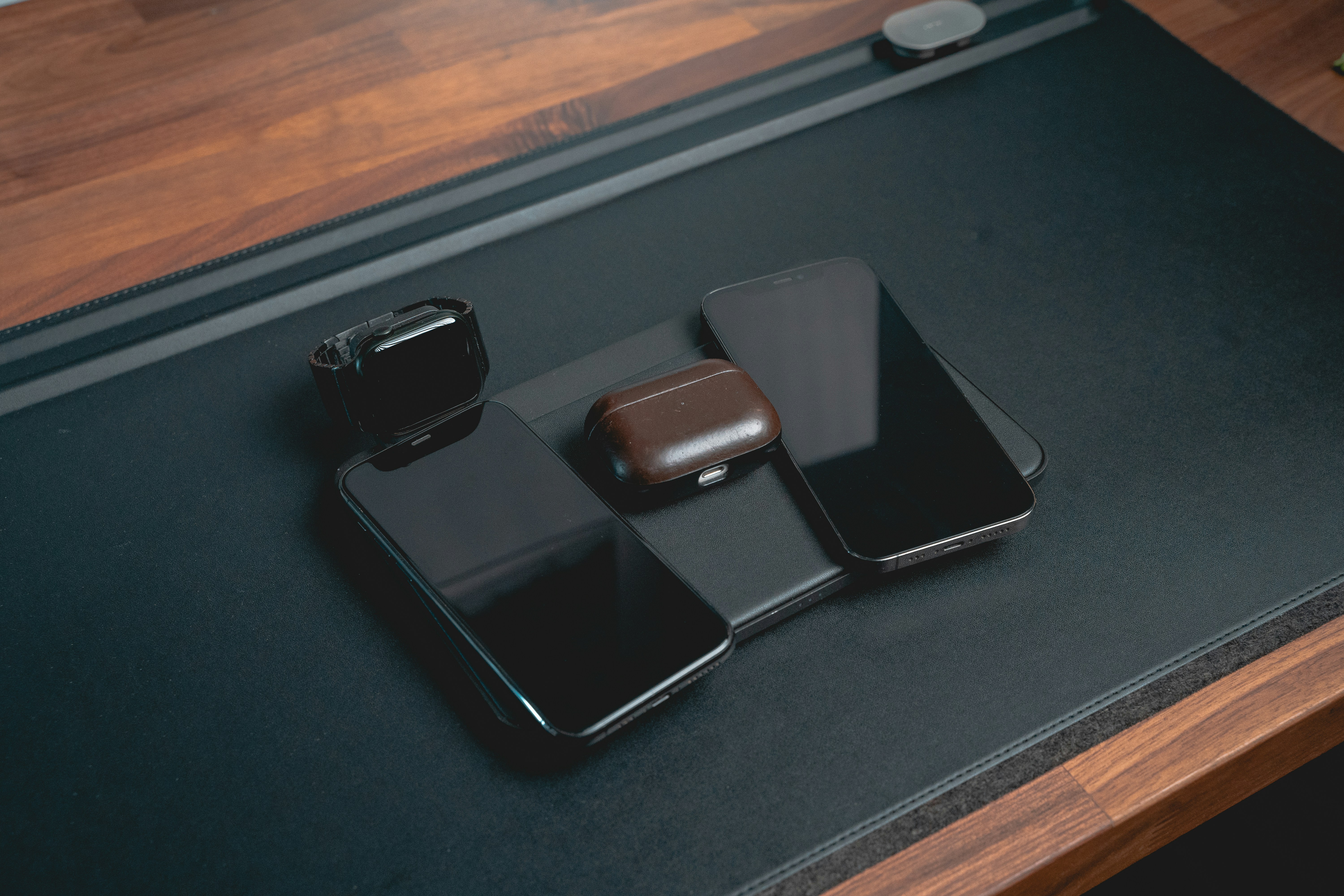 modern silver smartphone resting on a dark polished office desk next to wireless earbuds