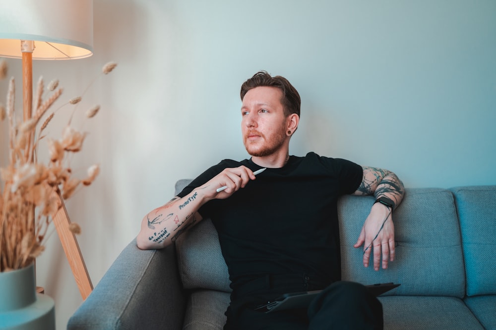a man sitting on a couch with tattoos on his arm